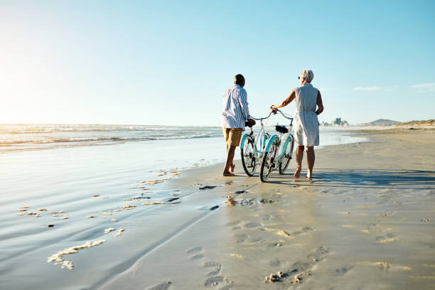 Deux personnes marchent sur la plage en poussant leur vélo. Une scène paisible qui illustre le mouvement doux, régulier, intégré au quotidien.