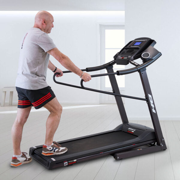 Homme montant sur le tapis de course Pioneer G6484H en se tenant aux barres de maintien latérales, accès arrière bas